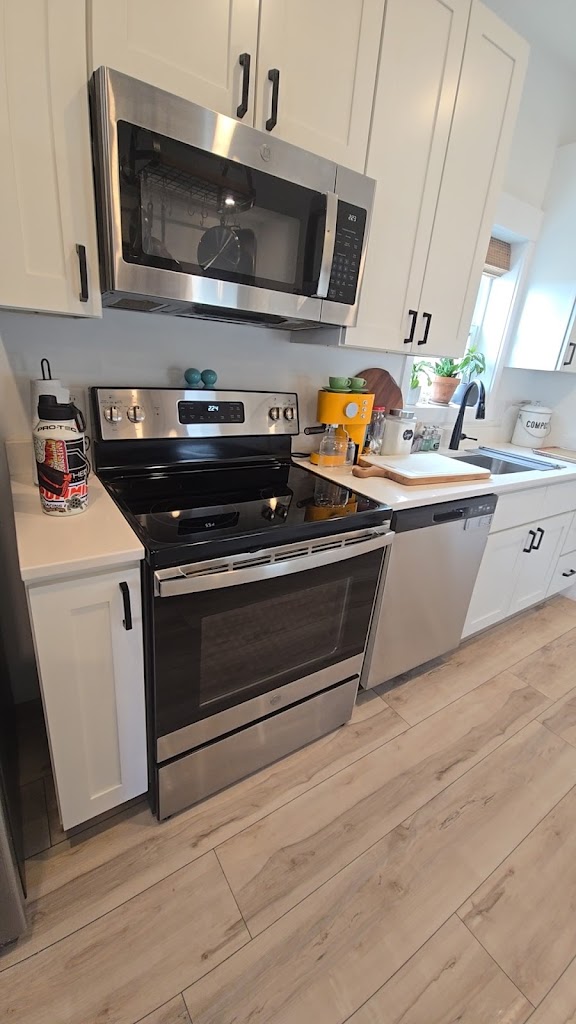 White kitchen cabinets surrounding a stainless steel range, microwave, and dishwasher